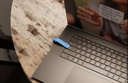 A WFH Privacy Clip in Blue clipped to a laptop keyboard on a stone table